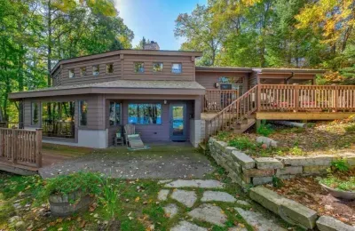 Lakeside view of the Peninsula Lakehouse and the expansive wrap around deck and path leading to private lakes access, boat dock, swimming area, and lake side fire pit.