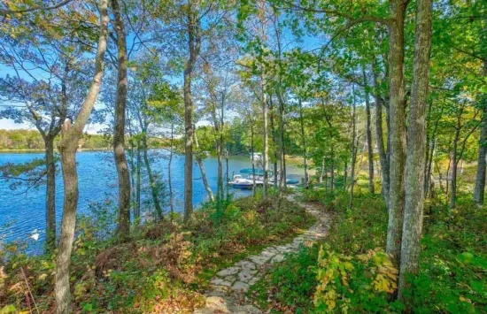 Well manicured lakeside pathway from the Peninsula Lakehouse down to the private boat, fire pit, and swimming dock along shallow sandy beach on crystal clear Little Round Lake with easy boat access to the entirety of Round Lake.