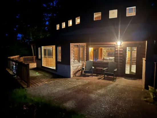 Nighttime lakeside view of the Peninsula Lakehouse and the expansive wrap around deck and path leading to private lakes access, boat dock, swimming area, and lake side fire pit.
