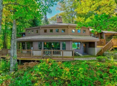 Lakeside view of the Peninsula Lakehouse and the expansive wrap around deck and path leading to private lakes access, boat dock, swimming area, and lake side fire pit.