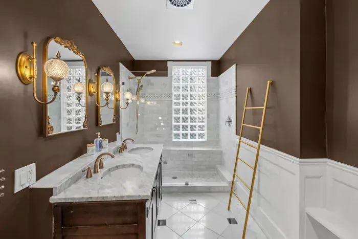 Featuring double vanities, vintage wall mirrors, three wall sconce lights, walk-in shower, custom tilework, towel ladder, full dressing mirror
