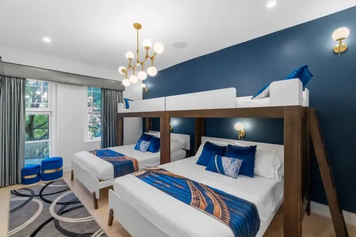 This designer suite features two queen beds and two twin heavy duty bunk beds, a globe chandelier, an ensuite bath, Roku 55'' Smart TV, leafy window views, four wall lights, and luggage rack. 