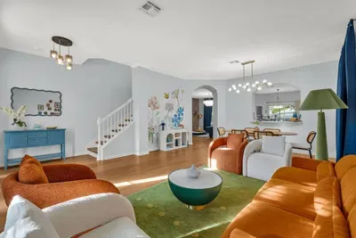 Living Room: Open-concept lounge with burnt-orange armchairs and a green rug, flowing into the dining area and staircase!