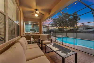 Screened Patio: Cozy lounge seating under twinkling string lights overlooks the sparkling pool at dusk!