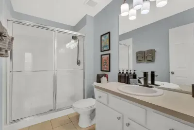 Full Bathroom 2: Glass walk-in shower, soft blue walls, EPCOT-inspired travel art, and a vanity stocked with shampoo, conditioner, and body wash!