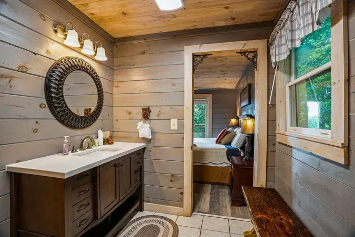 Rustic cabin bath with wood finishes, natural light, and cozy bedroom access
