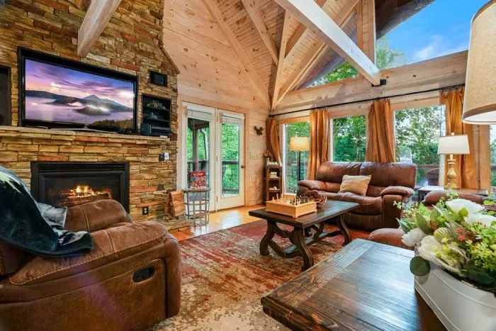 Cozy cabin living room with stone fireplace, vaulted ceilings, and forest views