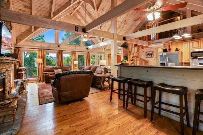 Rustic great room with vaulted ceilings, fireplace, and forest views