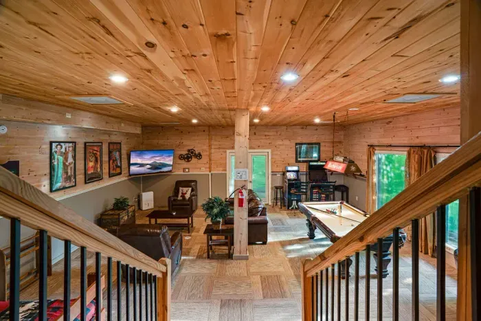 Cozy wood-paneled game room with pool table, arcade games, and lounge seating