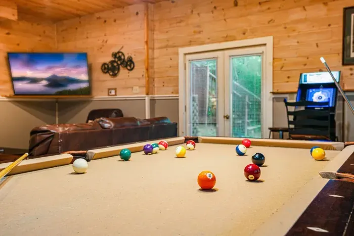 Rustic game room with pool table, arcade, TV, and cozy lounge seating
