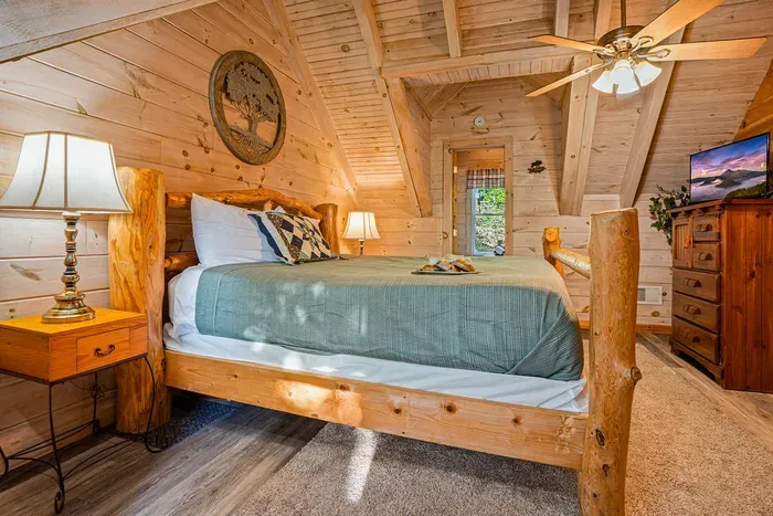 Cozy rustic cabin bedroom with log bed, vaulted wood ceilings, and TV