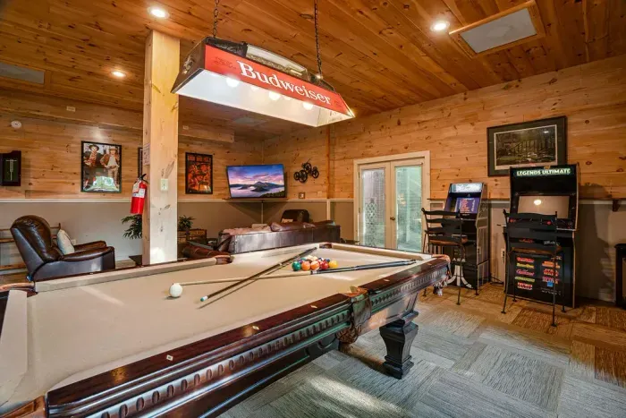 Rustic game room with pool table, arcade machine, TV, and cozy lounge seating
