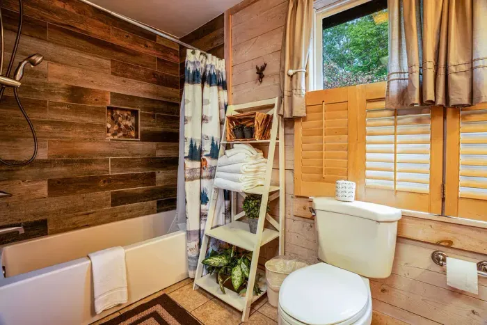 Rustic wood-paneled bathroom with tub, natural light, and cozy cabin charm