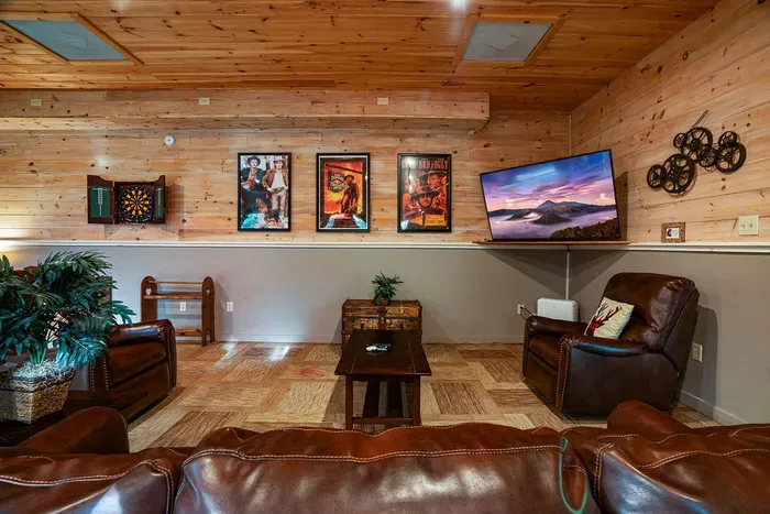 Cozy cabin-style media room with leather seating, TV, and dartboard