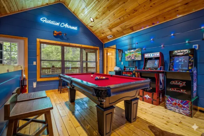 Rustic cabin game room: red‑felt pool, classic arcades, forest views.
