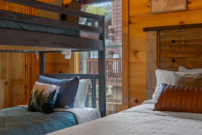 Cozy cabin bunk room with rustic wood, plush bedding, and a mountain view