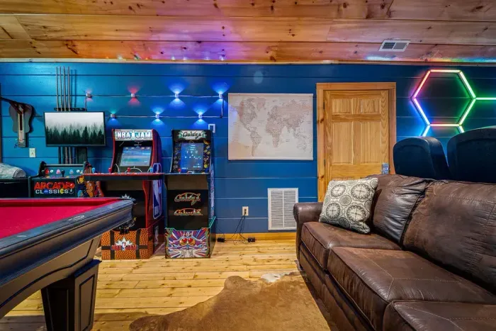 Vibrant cabin game room: arcades, pool table, LED accents, comfy sofa.