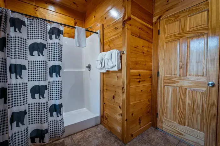 Cozy cabin bath with walk-in shower, warm wood walls, bear décor.