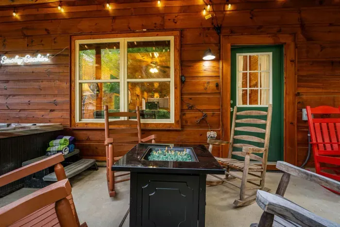 Cozy cabin porch with fire table, hot tub, string lights & rockers
