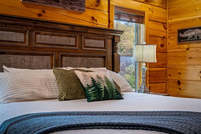 Cozy cabin bedroom with wooded views, plush bedding, and warm pine.