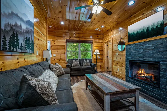 Cozy cabin living with stone fireplace, plush sofas, and forest views