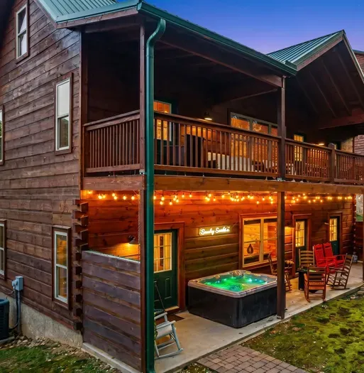 Rustic cabin with hot tub, string-lit patio & upper deck rocking chairs.