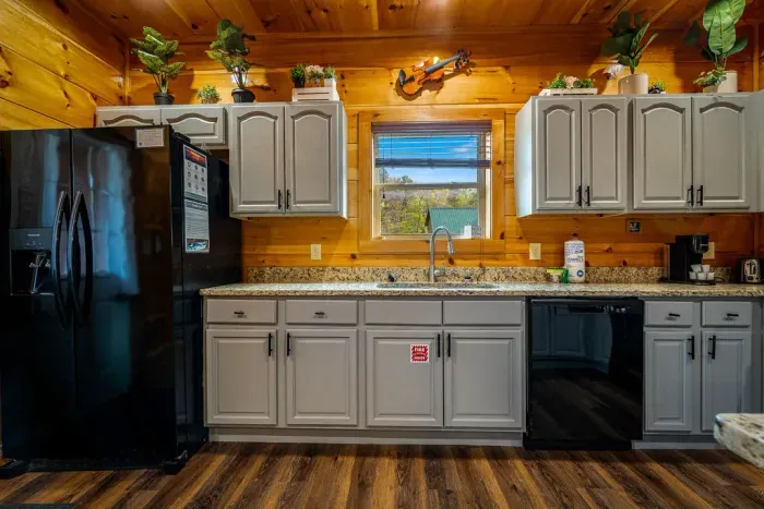 Rustic-chic cabin kitchen: granite counters, black appliances, window view.