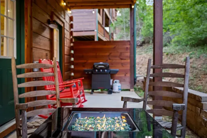 Wooded cabin patio with fire pit, rocking chairs, and BBQ grill