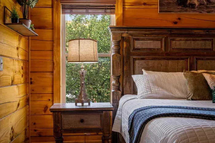 Cozy cabin bedroom with carved bed, forest view, and warm glow