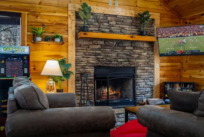 Cozy cabin lounge with stone fireplace, Pac‑Man arcade, and big-screen TV