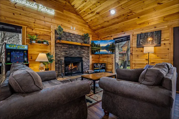 Cozy cabin lounge w/ stone fireplace, arcade, smart TV, vaulted wood ceiling