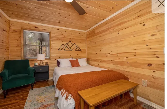 Cozy wood-paneled cabin room with queen bed, bench, and reading nook