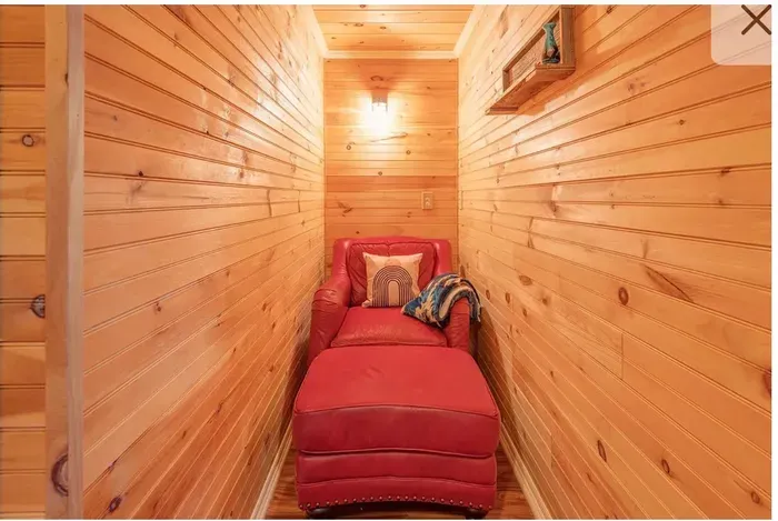 Cozy wood‑paneled reading nook with red chaise and warm sconce glow