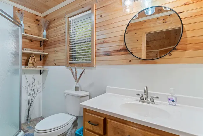Cozy wood-paneled bathroom with bright vanity and walk-in shower