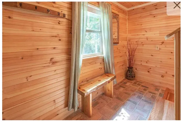 Sunny wood-paneled mudroom with rustic bench and brick floors