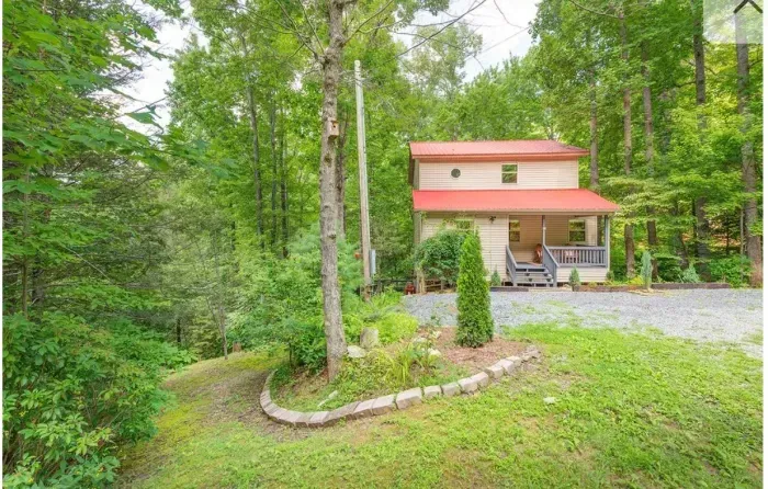 Private forest cabin with red roof, covered porch, and gravel drive