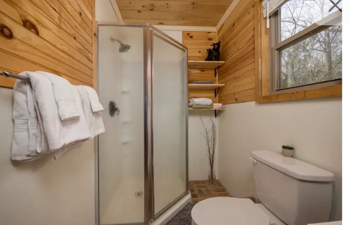 Cozy cabin bath with frosted shower, window light, and plush robes