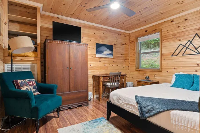 Cozy cabin-style bedroom with TV, desk, and warm wood interiors