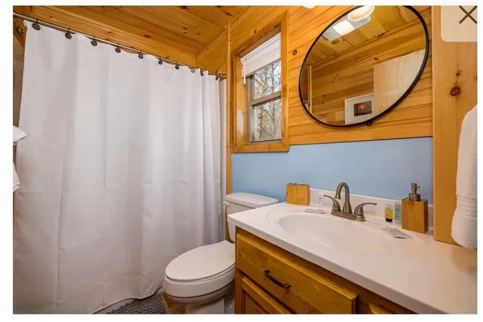 Cozy cabin bath with window light, tub/shower, and stocked vanity.