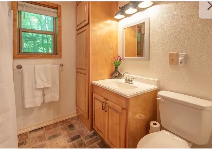 Cozy, wood-accent bath with stone floor and forest-view window