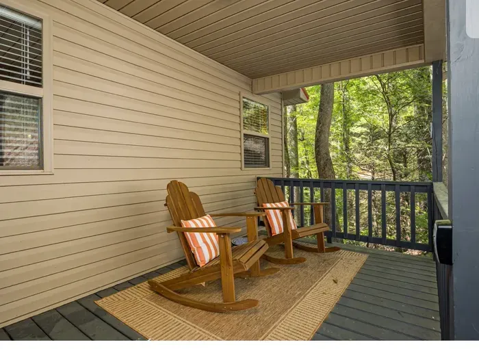 Covered porch with rocking chairs, side table, and tranquil forest view