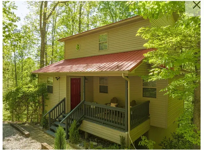Cozy forest cabin with red metal roof and covered porch seating