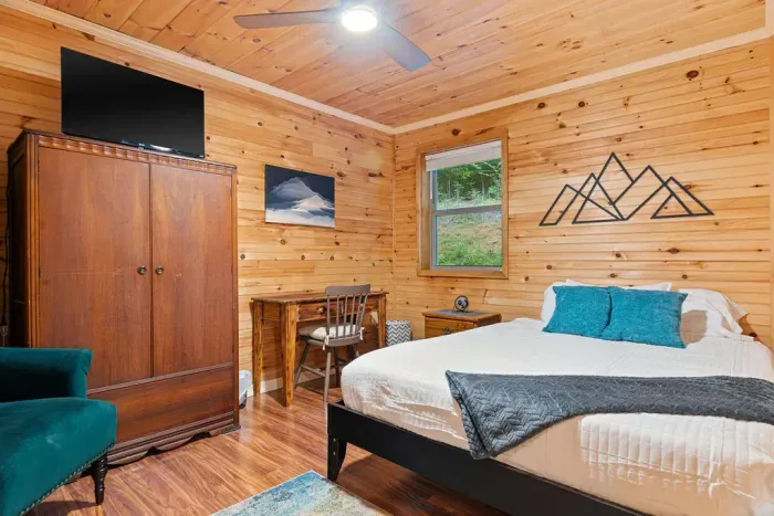 Cozy wood-paneled bedroom with queen bed, desk, TV, and serene nature views