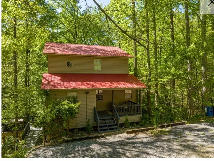 Secluded forest cabin with red roof, cozy porch, and gravel parking