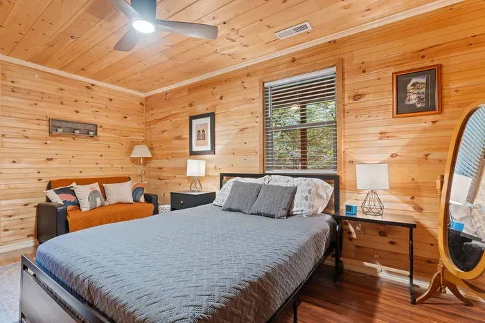 Cozy cabin-style bedroom with plush bed, sofa, and peaceful wooded views