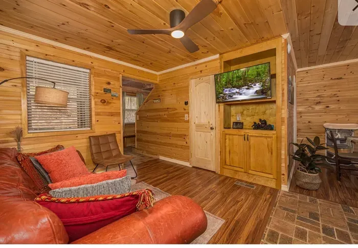 Cozy wood-paneled cabin lounge with smart TV, ceiling fan, and dining nook