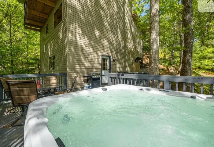Forest-view deck with hot tub, grill, and outdoor dining.