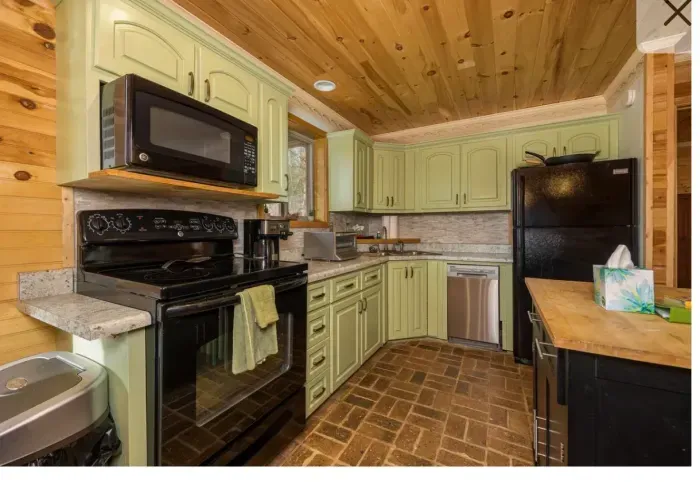 Charming cabin kitchen with mint cabinets, brick floor, and modern appliances