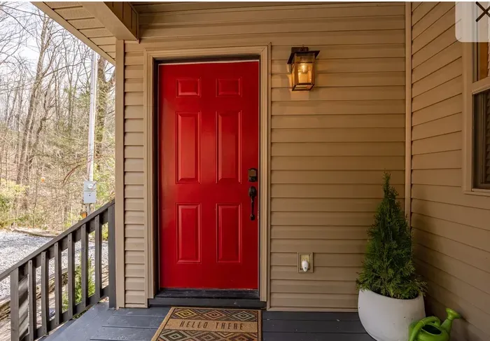 Welcoming red door and cozy porch with lantern, planter, forest views