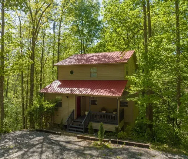 Secluded forest cabin with red roof, rocking-chair porch, and easy parking.